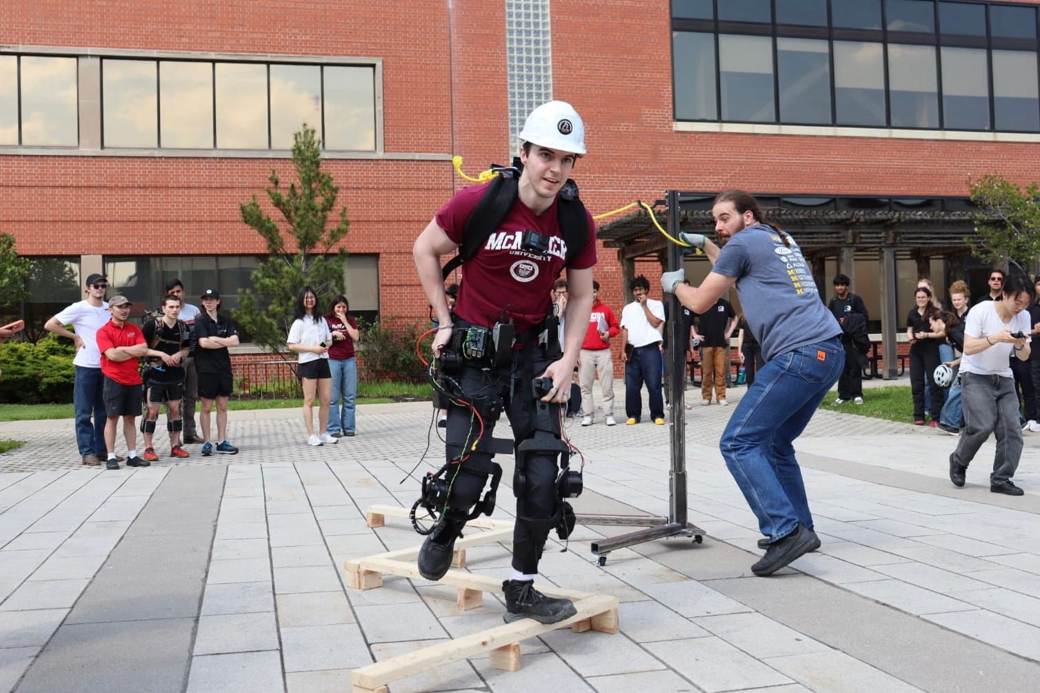 A McMaster pilot navigating a balance obstacle in the powered exoskeleton at ACE 2026, with teammates alongside.