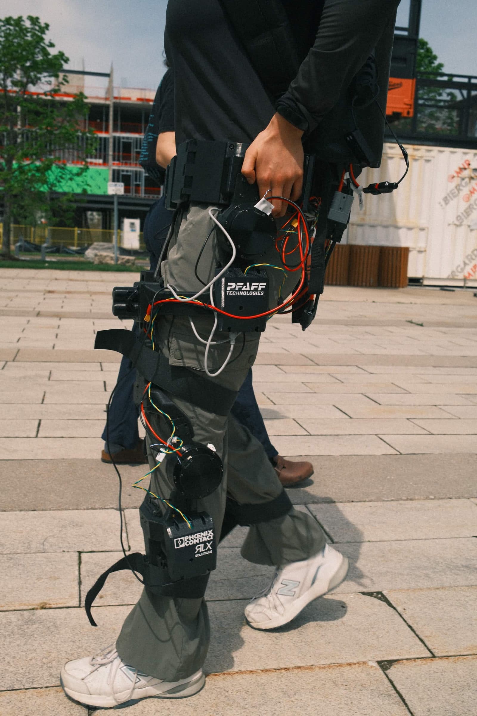 McMaster Exoskeleton team members working on the suit with sponsor logos displayed.